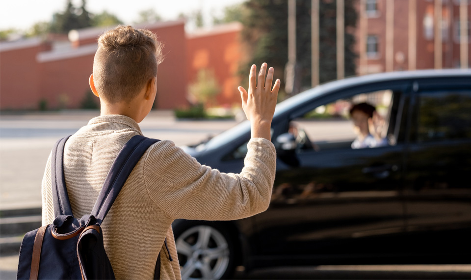 A student waving goodbye to parents after being dropped off at school.