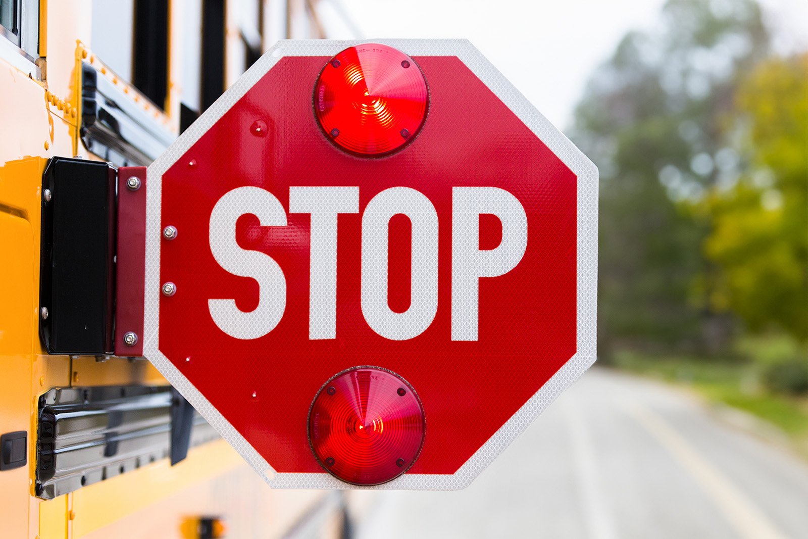 A close up of a stop sign attached to the side of a yellow school bus.